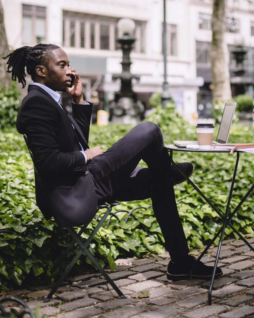 A business owner taking a call at an outdoor cafe table with a laptop and notebook